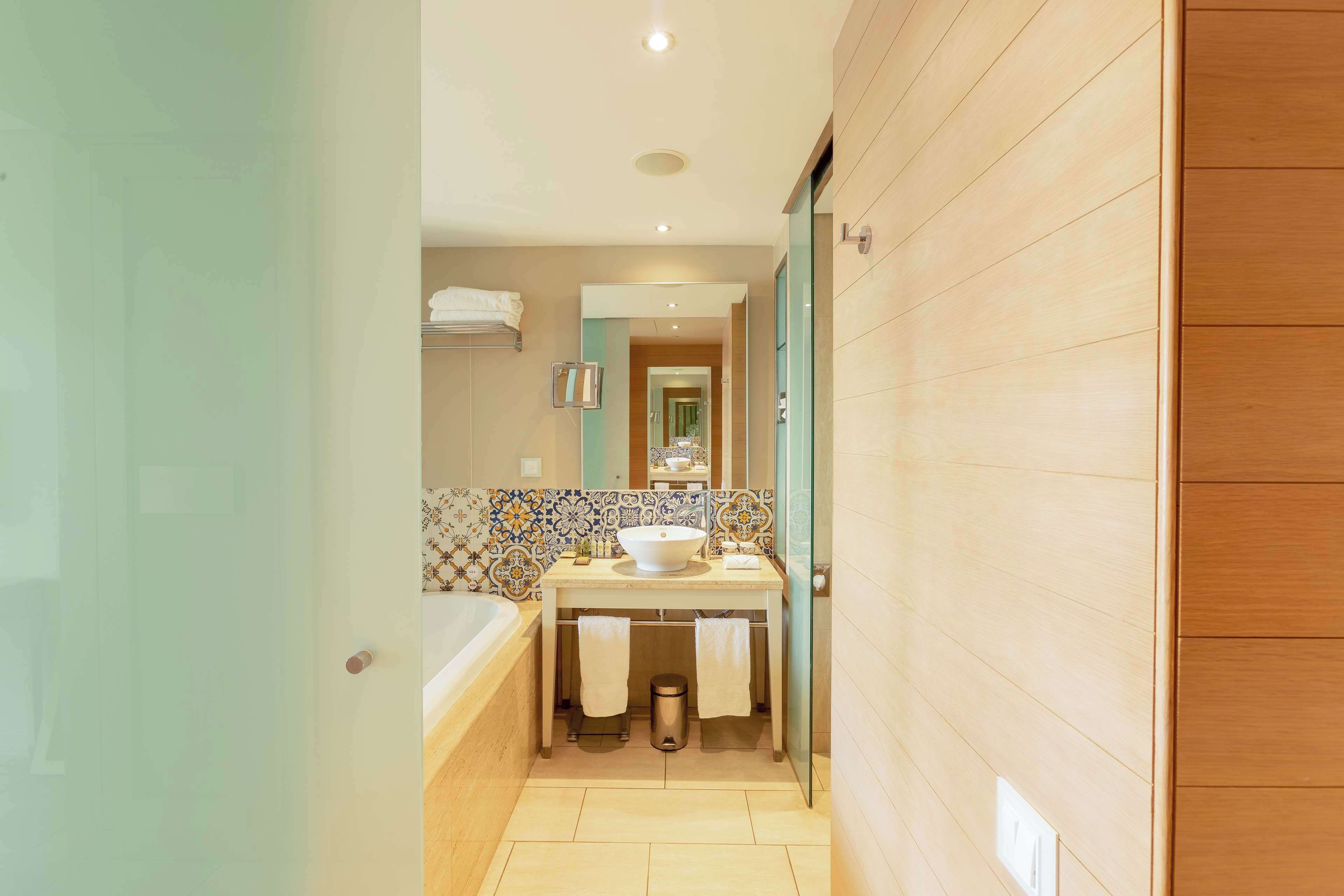 Une salle de bain moderne avec une baignoire, un lavabo doté d’un grand miroir et un mur recouvert de carreaux.