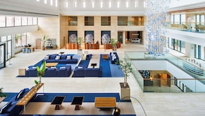 A spacious lobby with multiple seating areas, a central decorative plant arrangement, and a modern chandelier. - Hilton Vilamoura As Cascatas Golf Resort & Spa (Loulé)