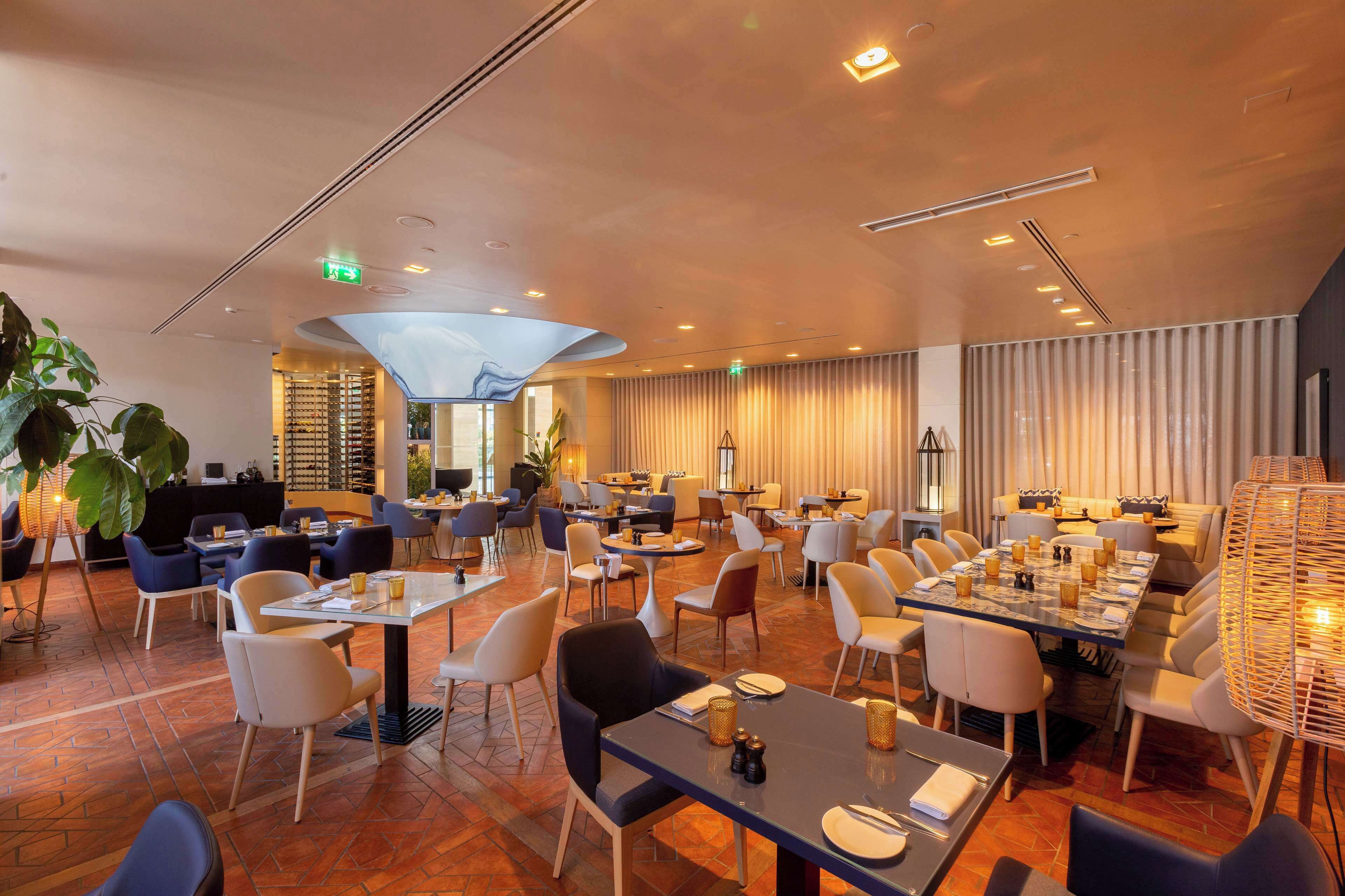 Ein geräumiges Restaurant mit verschiedenen Essbereichen, darunter eine Bar und ein Sitzbereich mit einer großen Pflanze.