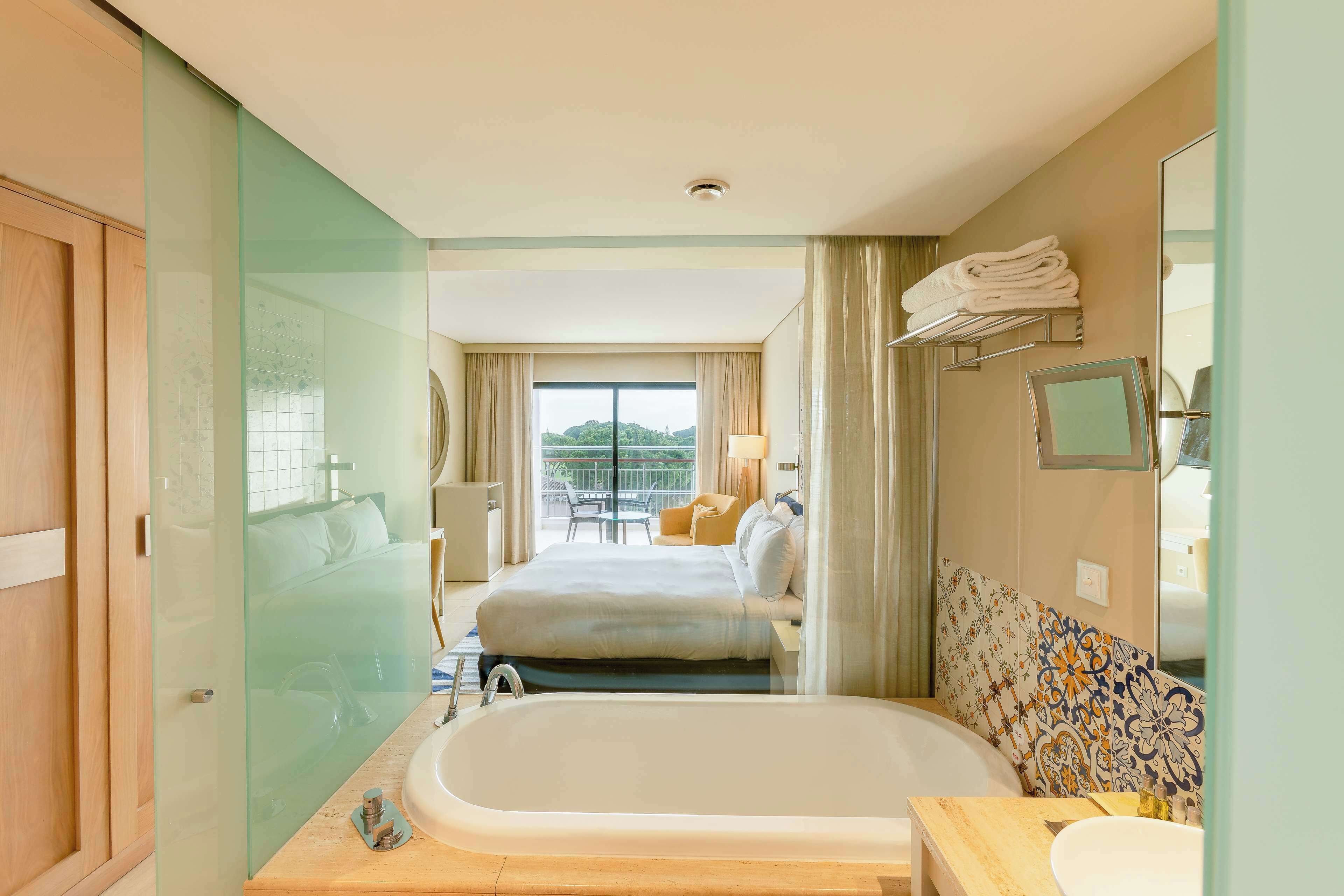 Una habitación de hotel con una cama grande, una bañera, un lavamanos y un balcón con vistas.