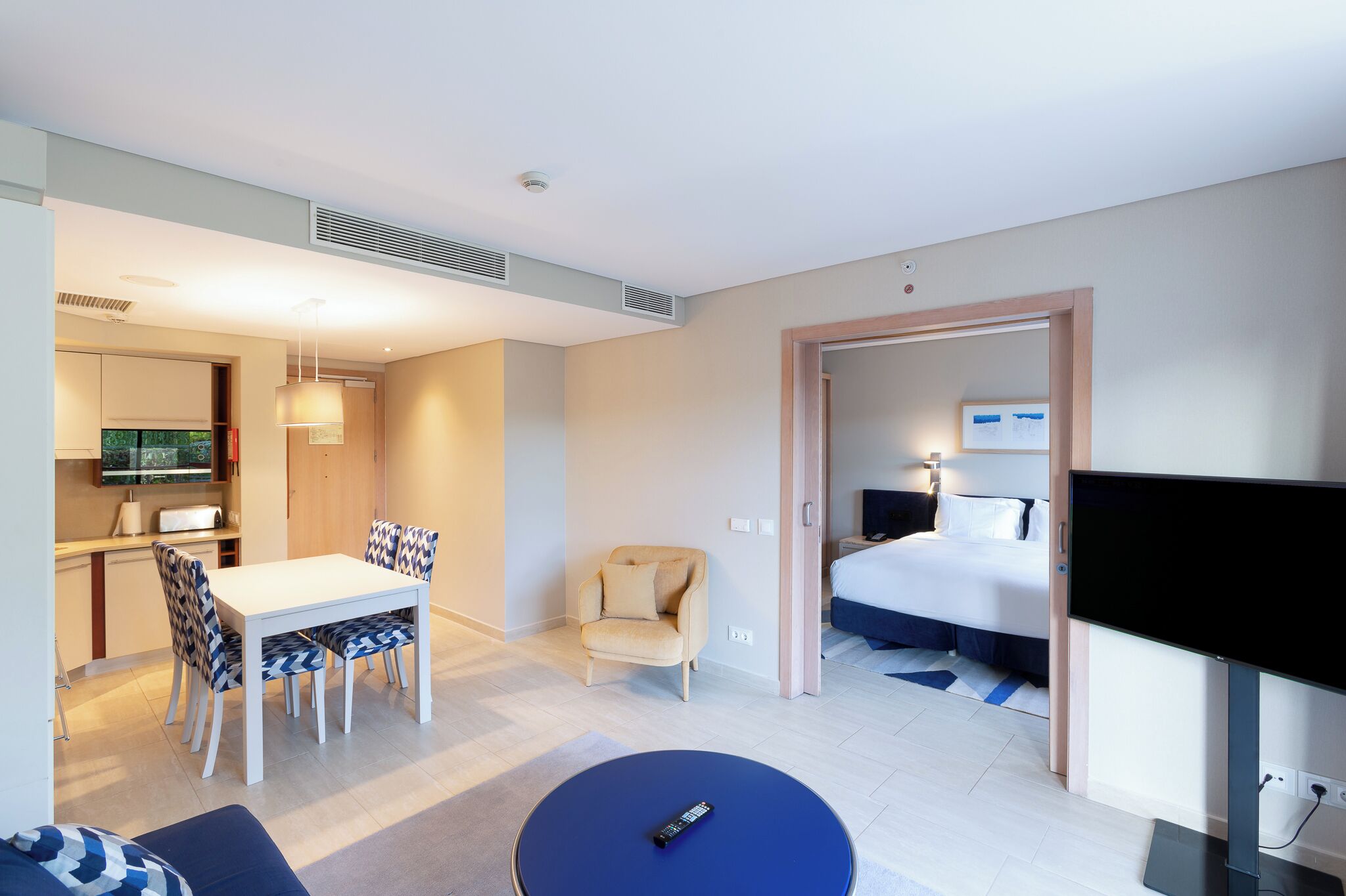 A modern hotel room with a dining area, a sofa, a TV, and a bed.