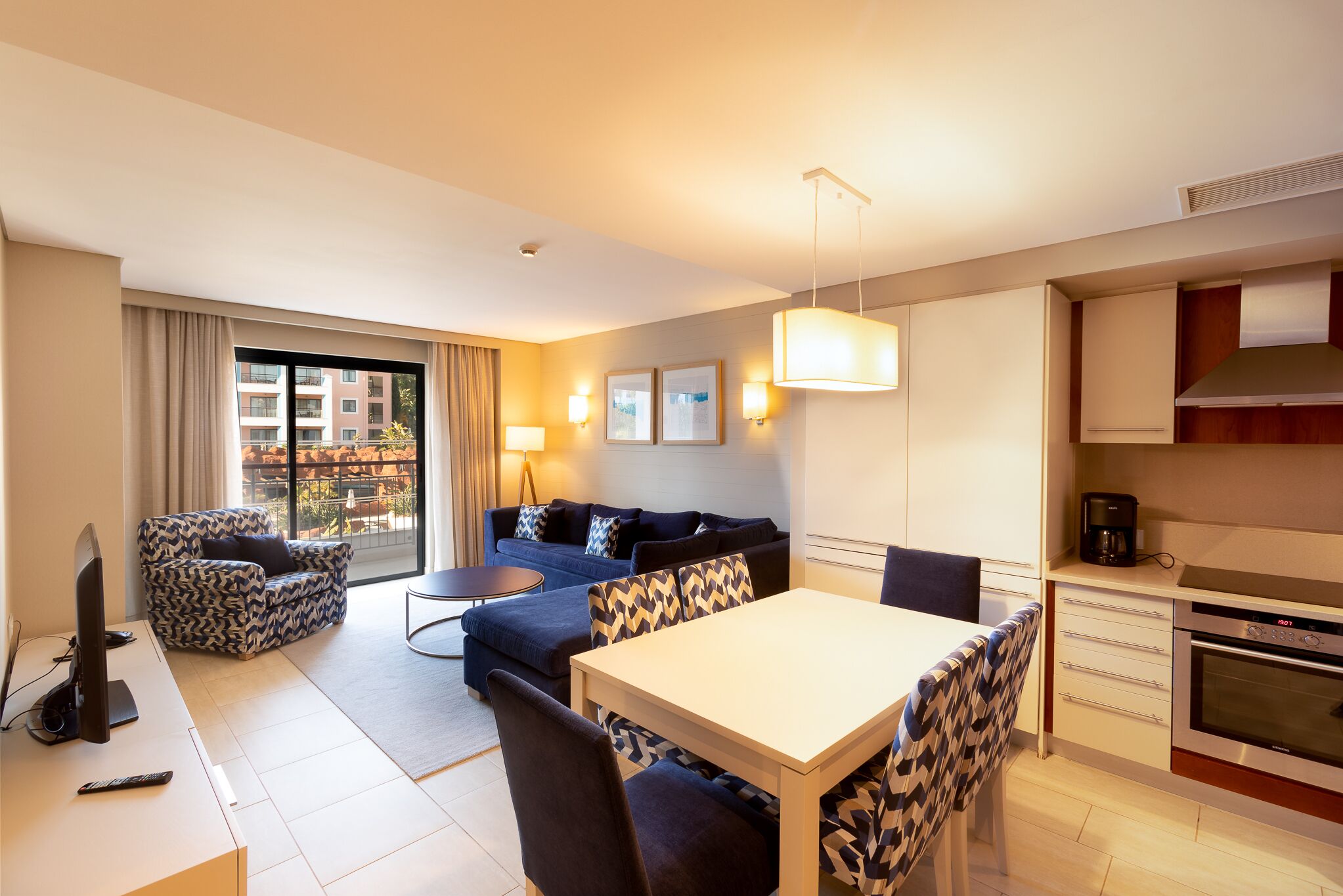 Ein modernes Hotelzimmer mit Sofa, Esstisch und Küchenzeile.