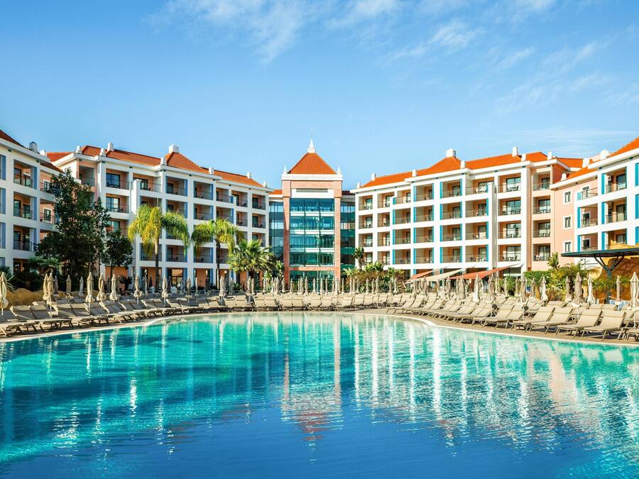 Hotel amb una gran piscina, múltiples balcons i un edifici central de vidre.
