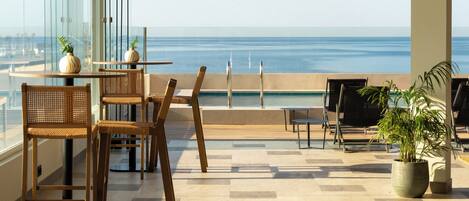 A terrace with a view of the ocean, featuring a table with chairs, a potted plant, and a seating area with a view.