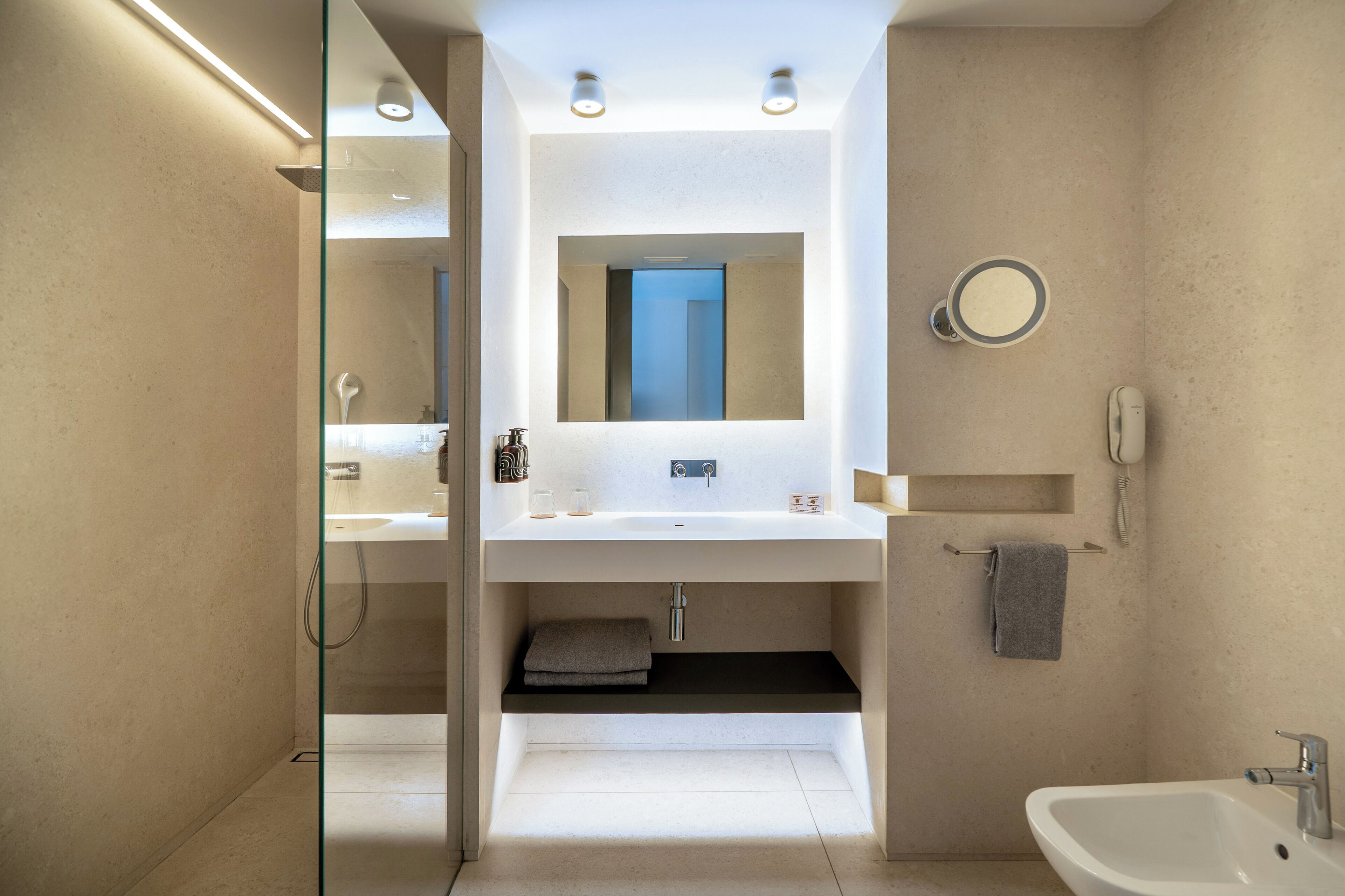 A modern bathroom with a glass-enclosed shower, a large mirror, a sink, and a bidet.