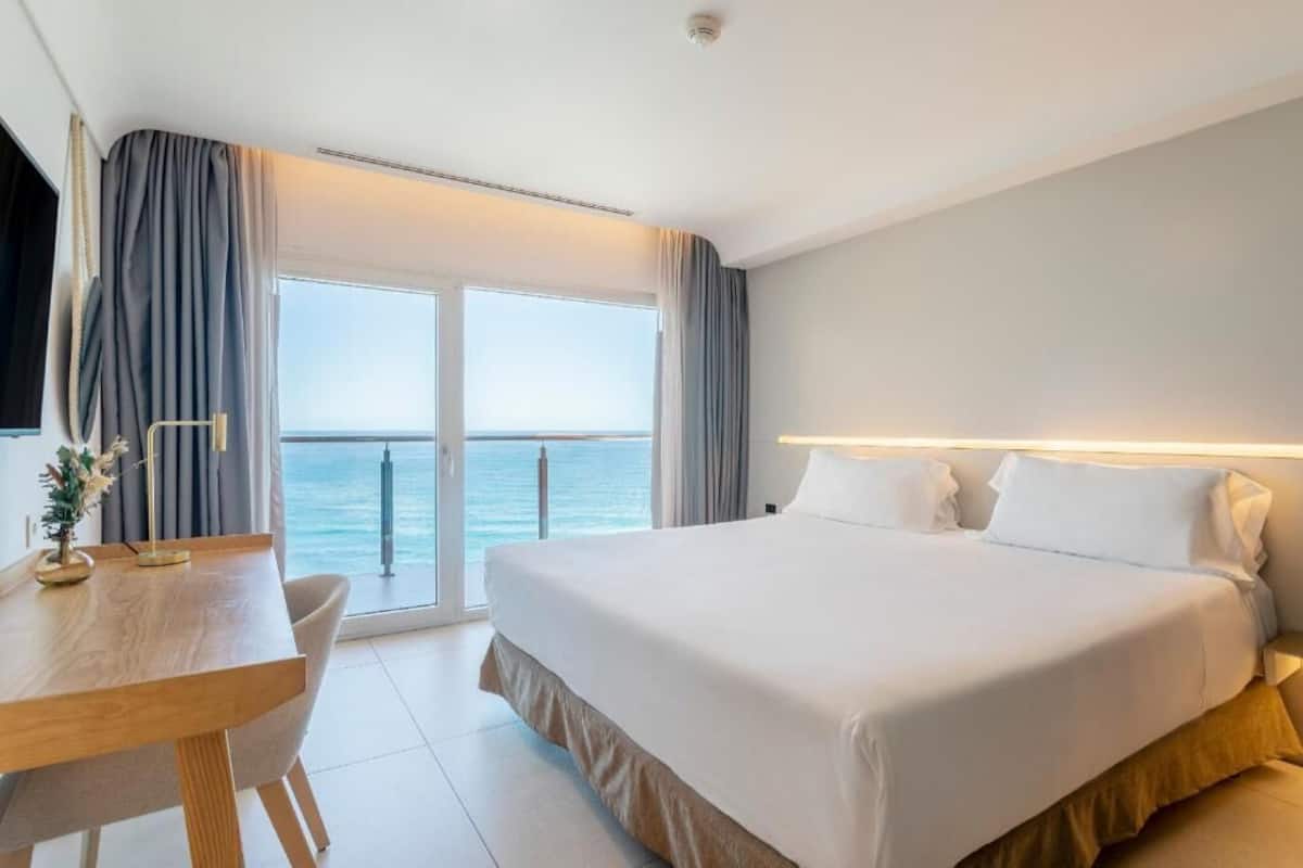 A hotel room with a bed, a desk, and a view of the sea.