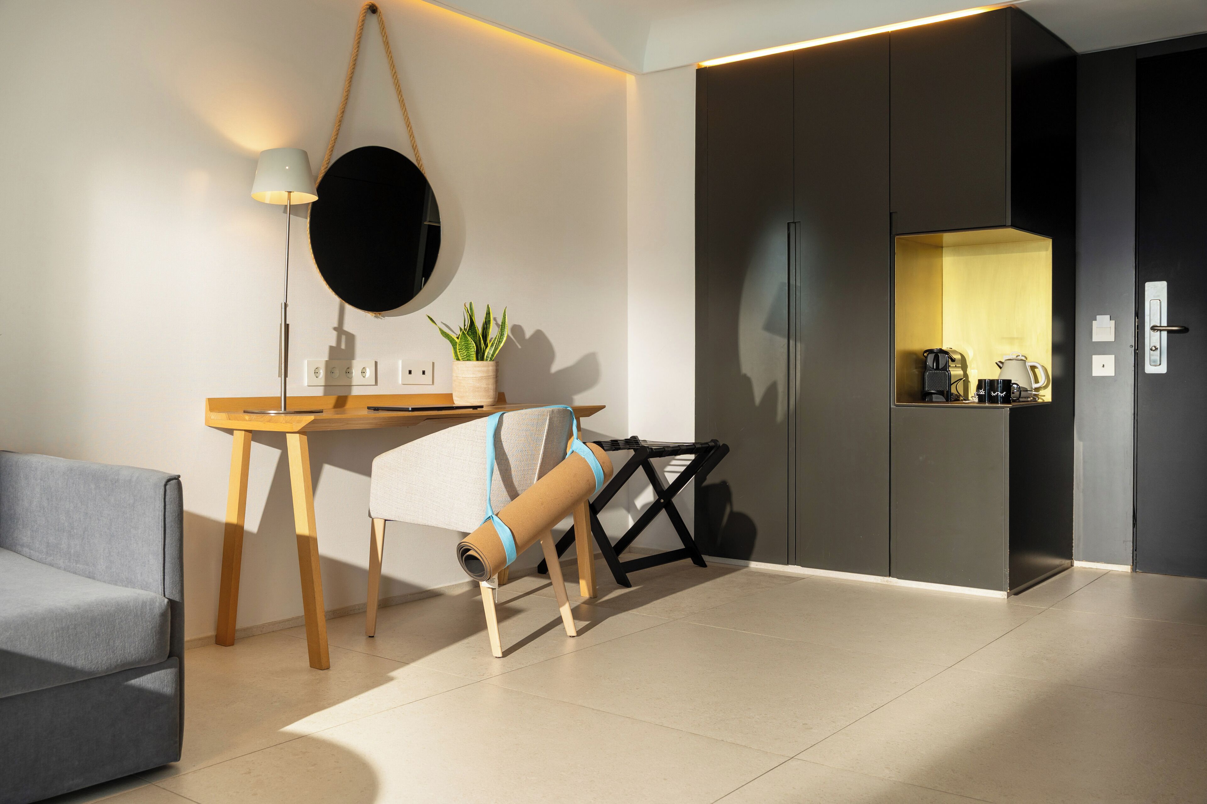 Una sala moderna con sofá, escritorio, lámpara, planta en maceta y una pequeña kitchenette.