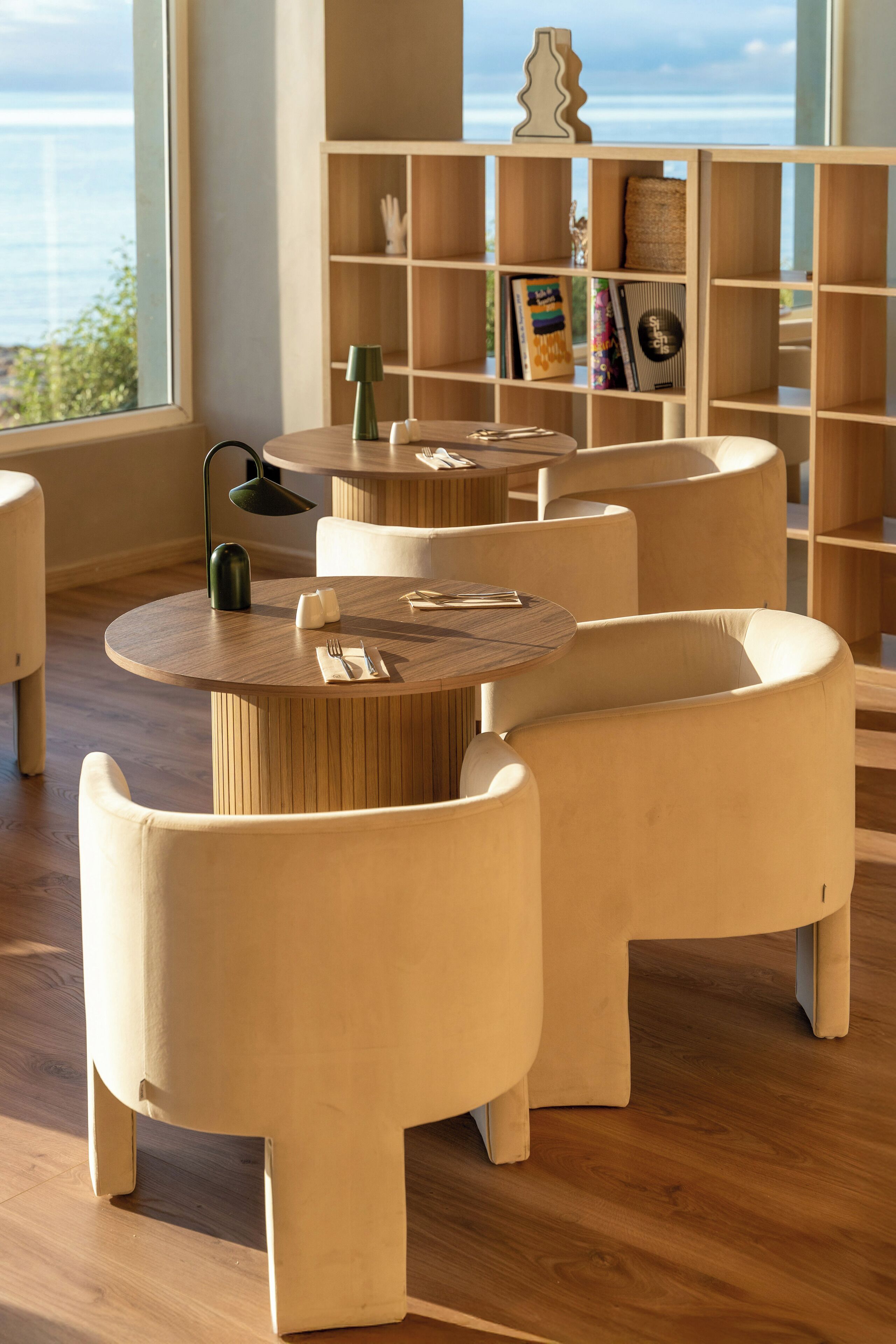 Een modern interieur met ronde tafels en comfortabele stoelen, houten vloeren en een boekenplank met diverse objecten.