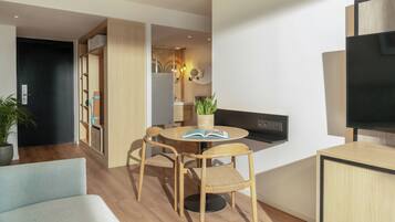Una sala de estar moderna con una mesa de comedor redonda, dos sillas de madera, un sofá, un televisor y una planta en maceta.