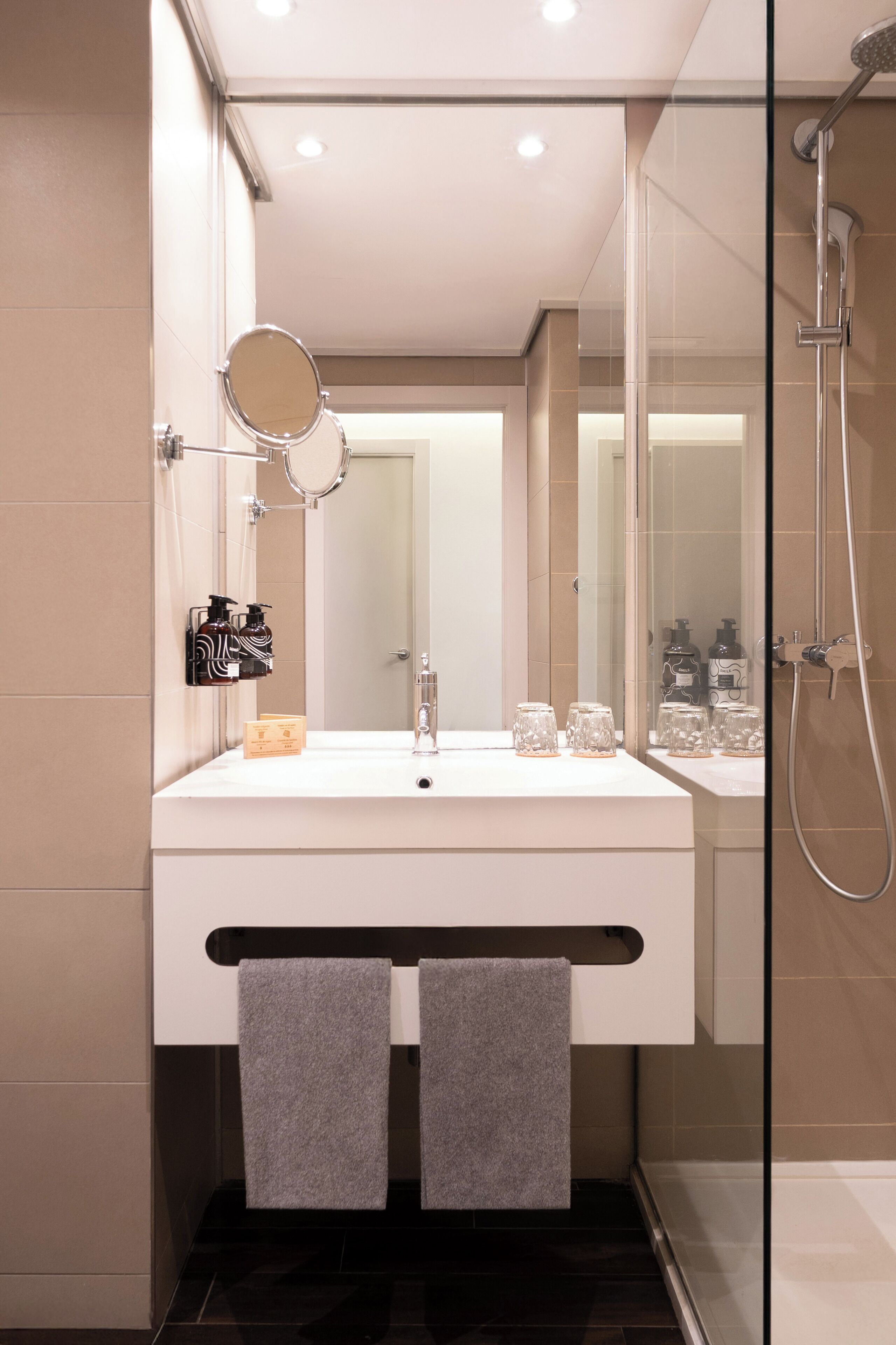 A modern bathroom with a large mirror, two towels, a glass shower enclosure, and a white sink.