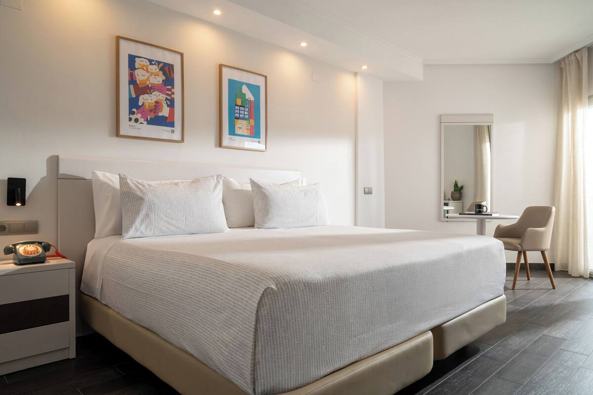 A modern hotel room with a large bed, bedside tables, a desk, and a mirror.