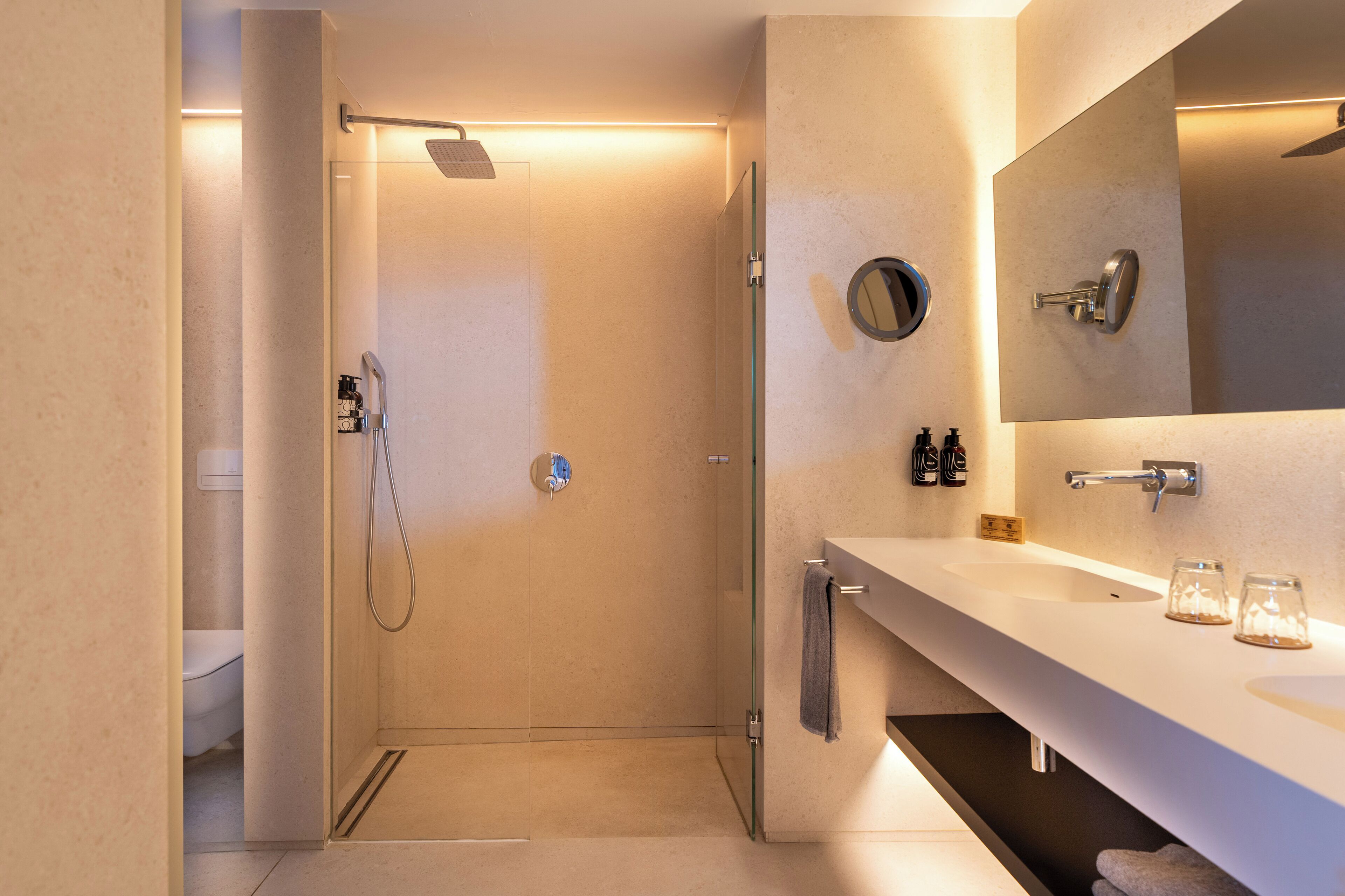 Un baño moderno con ducha de vidrio, un espejo grande y un tocador blanco con perchero.