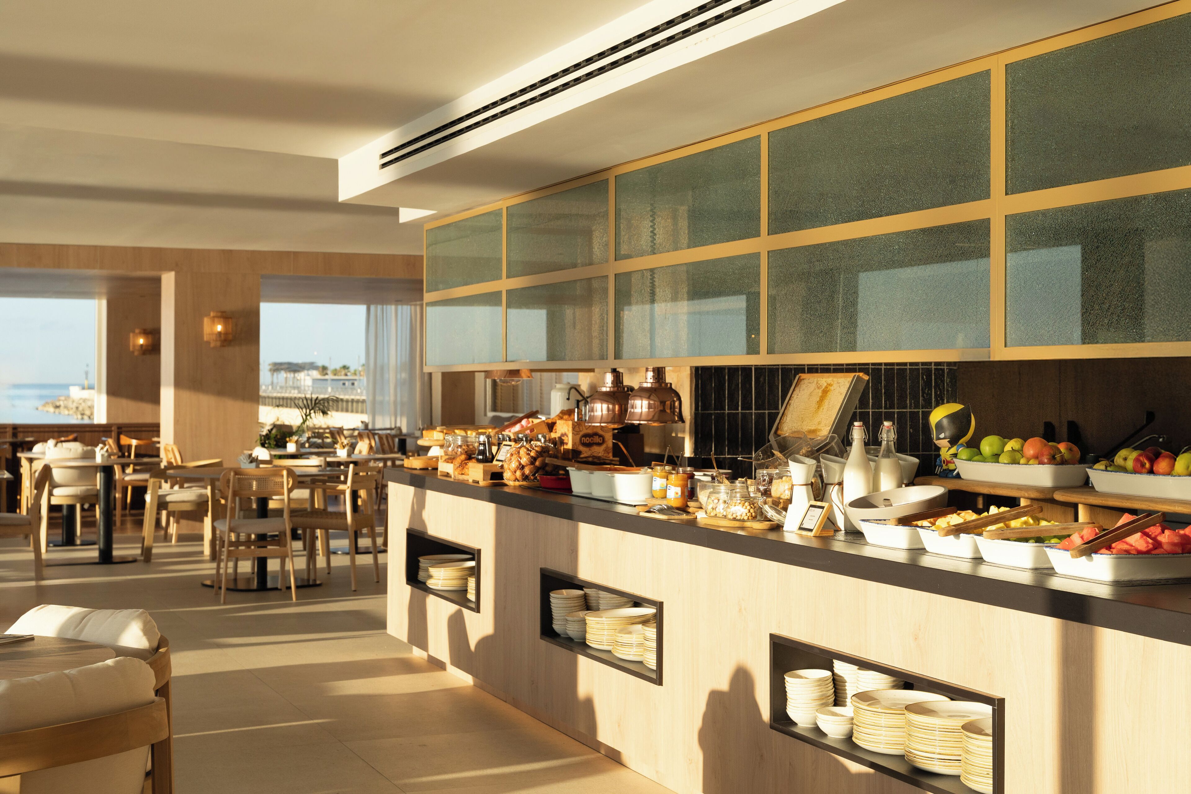 A modern breakfast bar with a view of the sea, wooden furniture, and a variety of breakfast items.