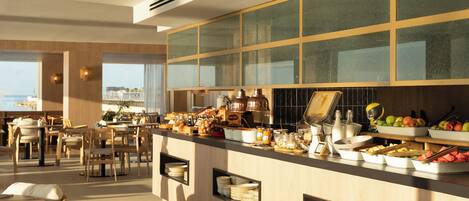 A modern breakfast bar with a view of the sea, wooden furniture, and a variety of breakfast items.