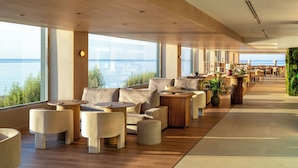 A spacious indoor area with seating arrangements and large windows overlooking the sea.
