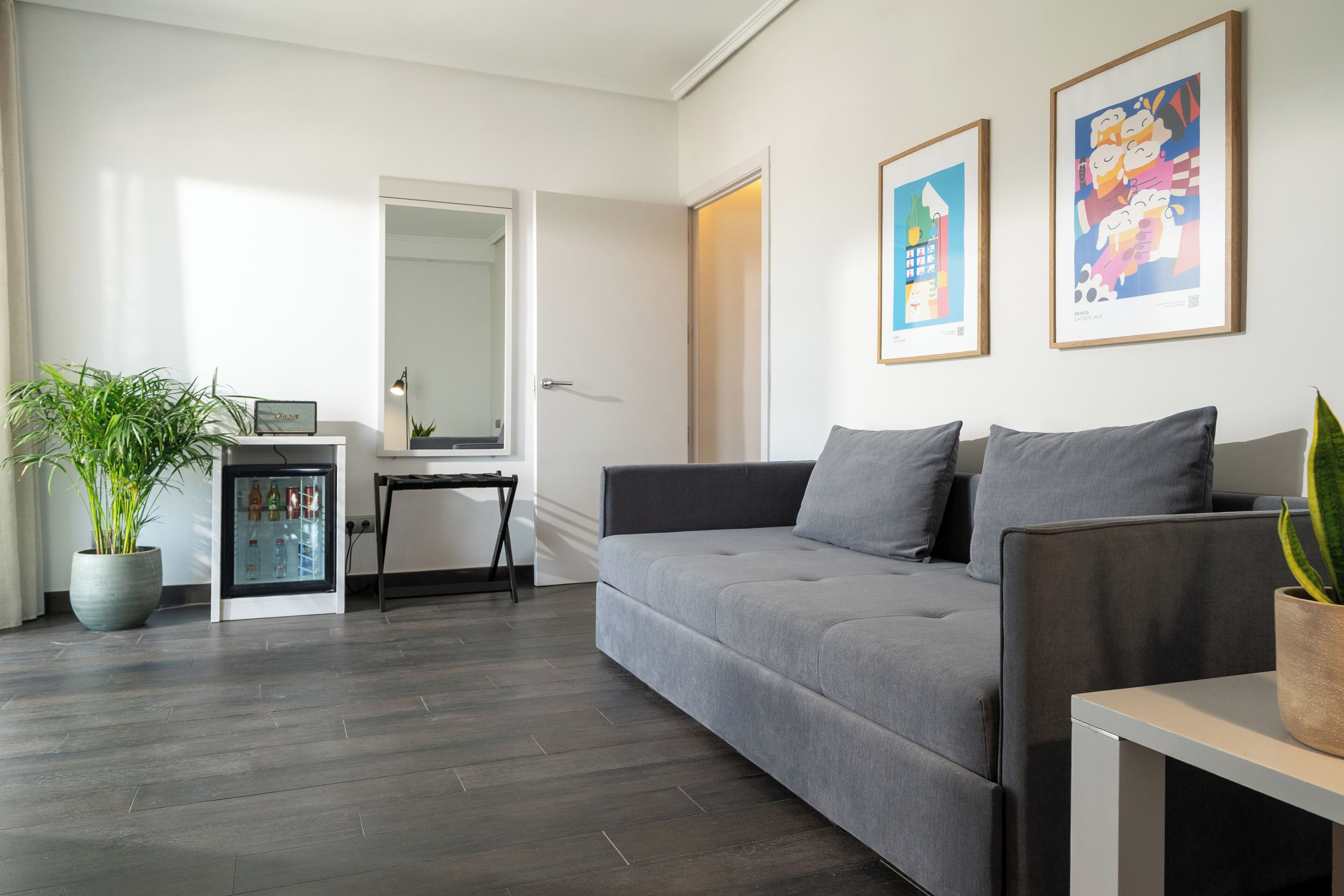 Een moderne woonkamer met een grijze bank, een bijzettafeltje, een potplant en een minibar.