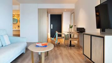 Una sala de estar moderna con un sofá azul claro, una mesa redonda con libros, un televisor sobre un mueble bajo y piso de madera.