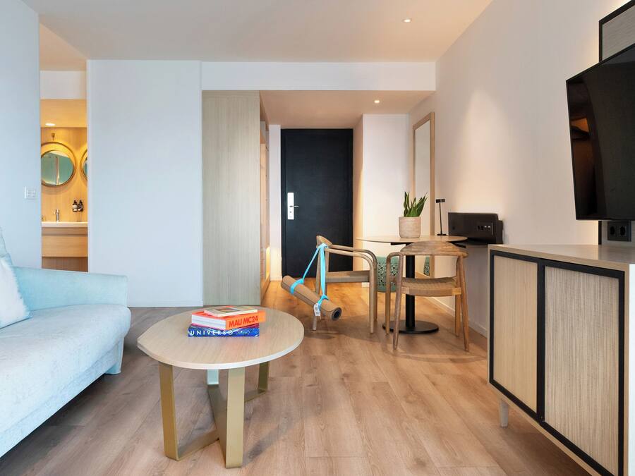 Una sala de estar moderna con un sofá azul claro, una mesa redonda con libros, un televisor sobre un mueble bajo y piso de madera.