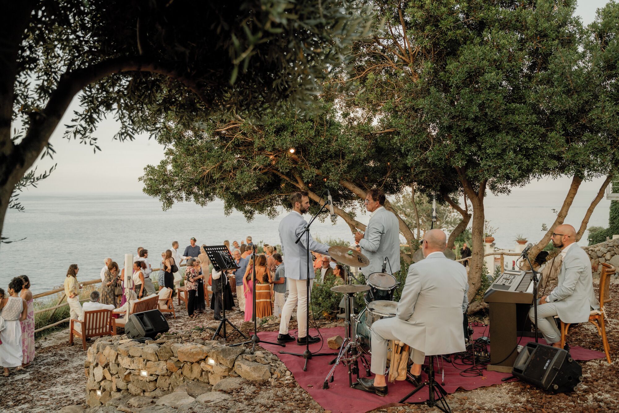 An outdoor music performance with musicians and an audience on a rocky shore.