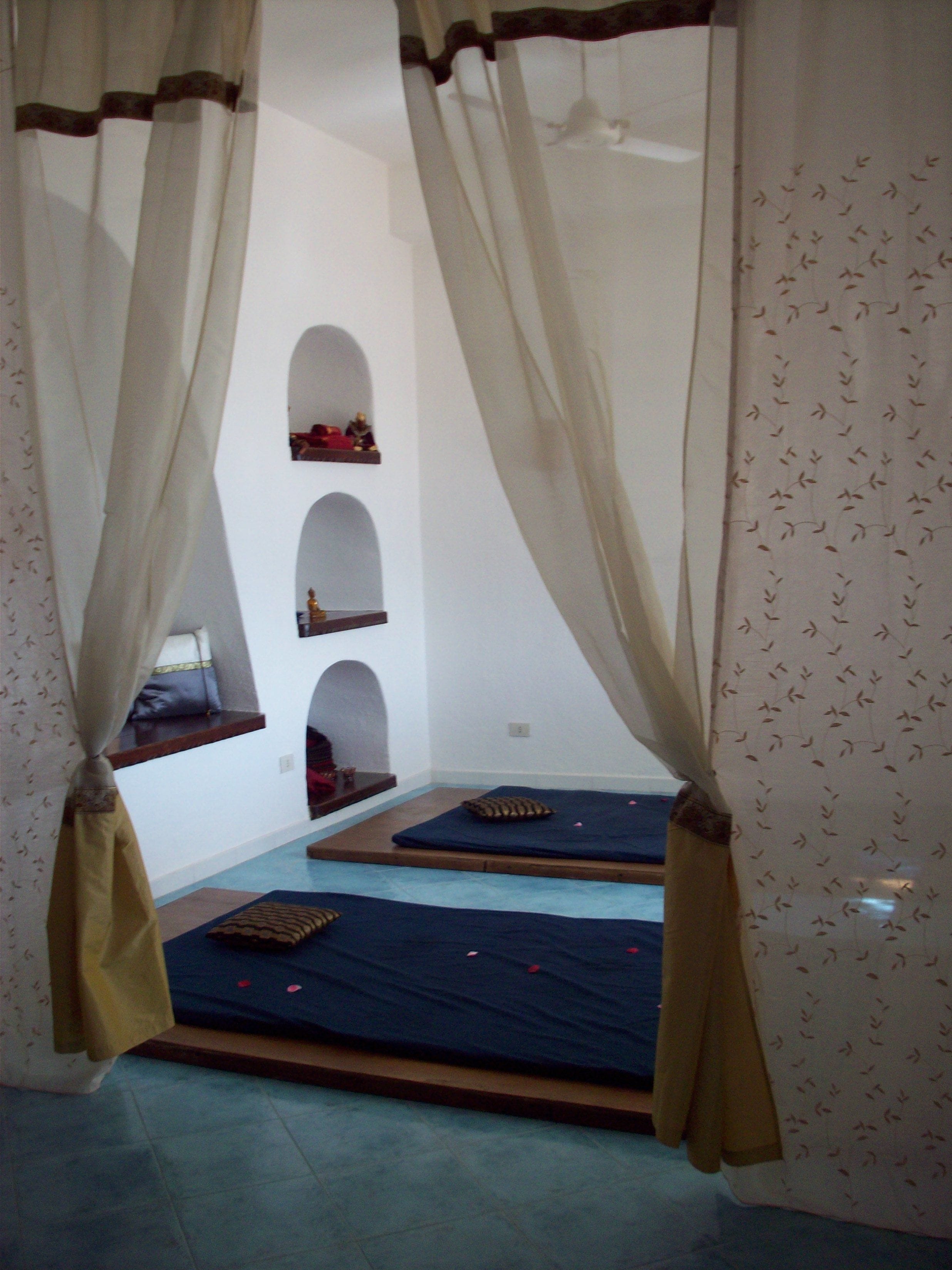 A room with two beds, a small window, and a wall with three arches.