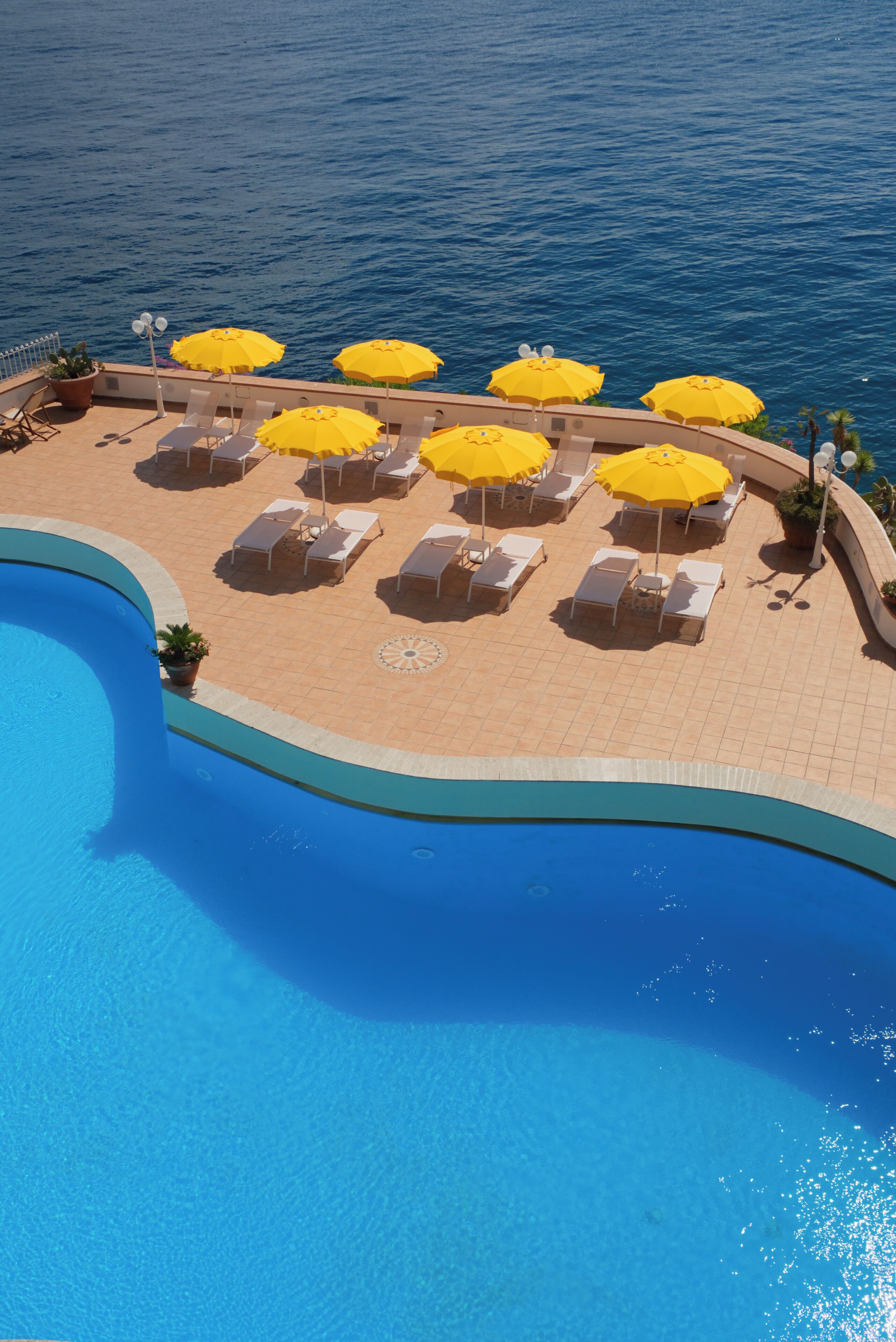 A poolside area with sun loungers and yellow umbrellas, overlooking a body of water.