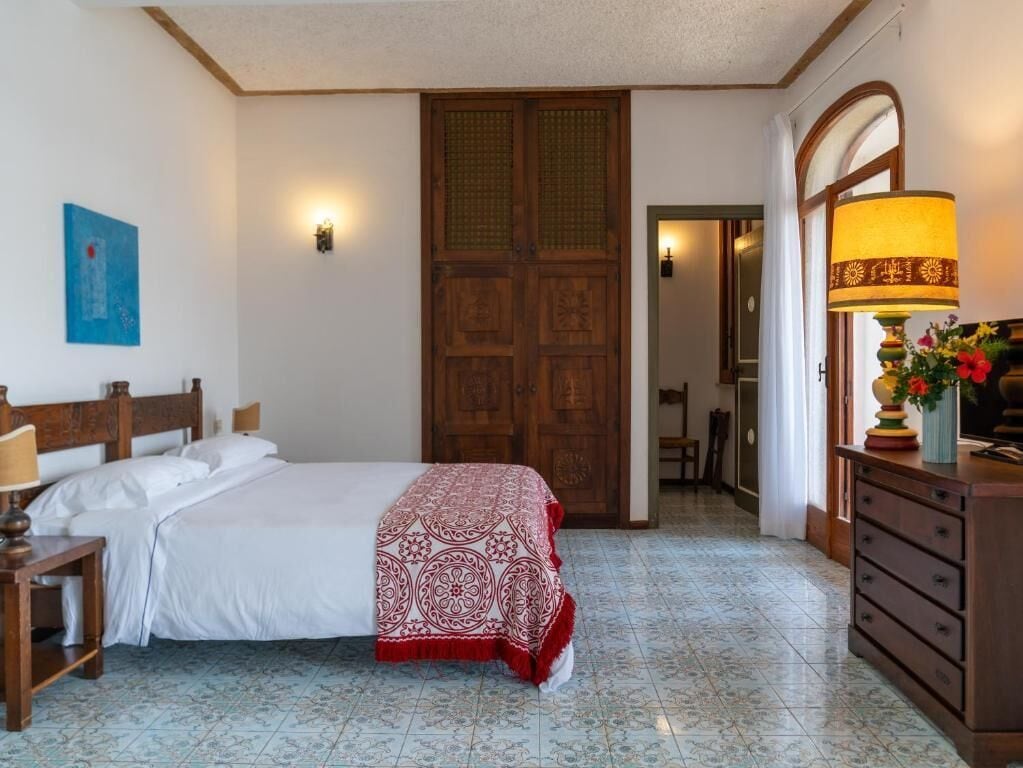 A bedroom with a bed, a dresser, a lamp, and a door.