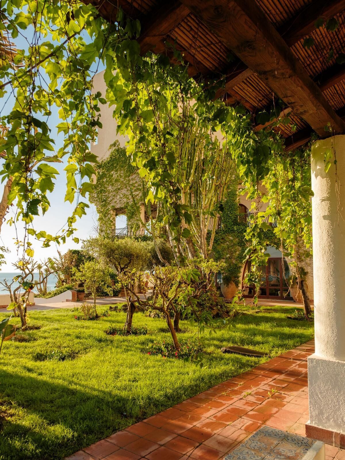 A covered outdoor area with a tiled pathway, greenery, and a building with a wooden roof.
