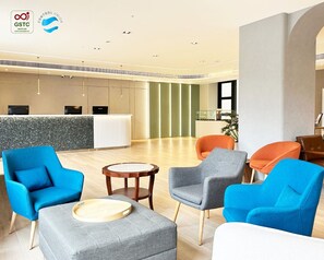 A modern hotel lobby with a reception desk, seating area with chairs, and a wooden floor.