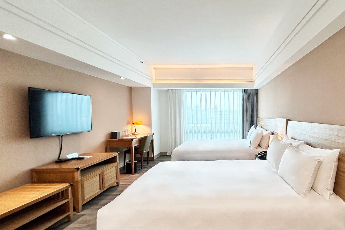A hotel room with a large bed, a desk with a chair, a television, and a window with curtains.