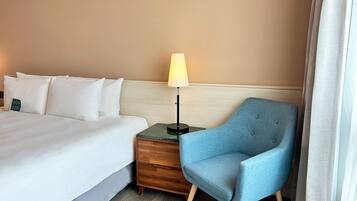 A hotel room with a bed, a nightstand, a lamp, a chair, and a window with curtains.