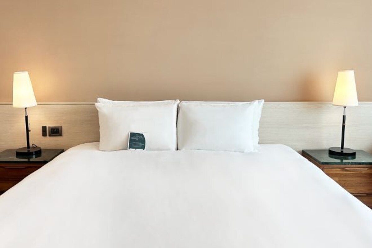 Un letto rifatto con lenzuola bianche, due abat-jour e un comodino con una lampada.