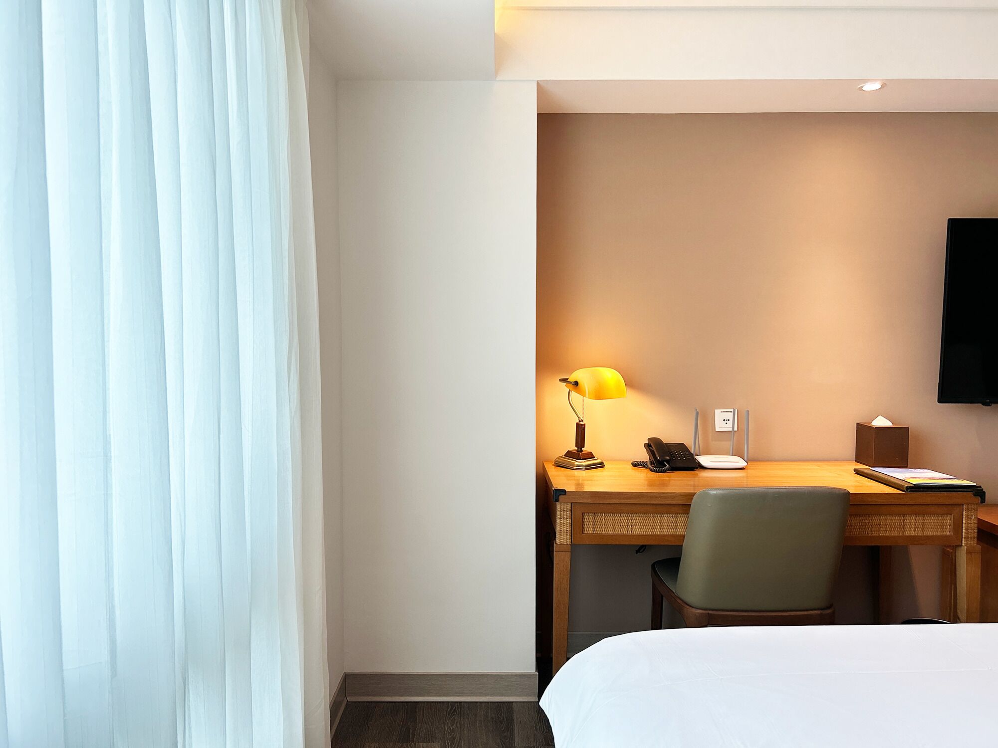 Une chambre d’hôtel équipée d’un lit, d’un bureau avec une lampe, d’une chaise et d’un téléviseur à écran plat fixé au mur.