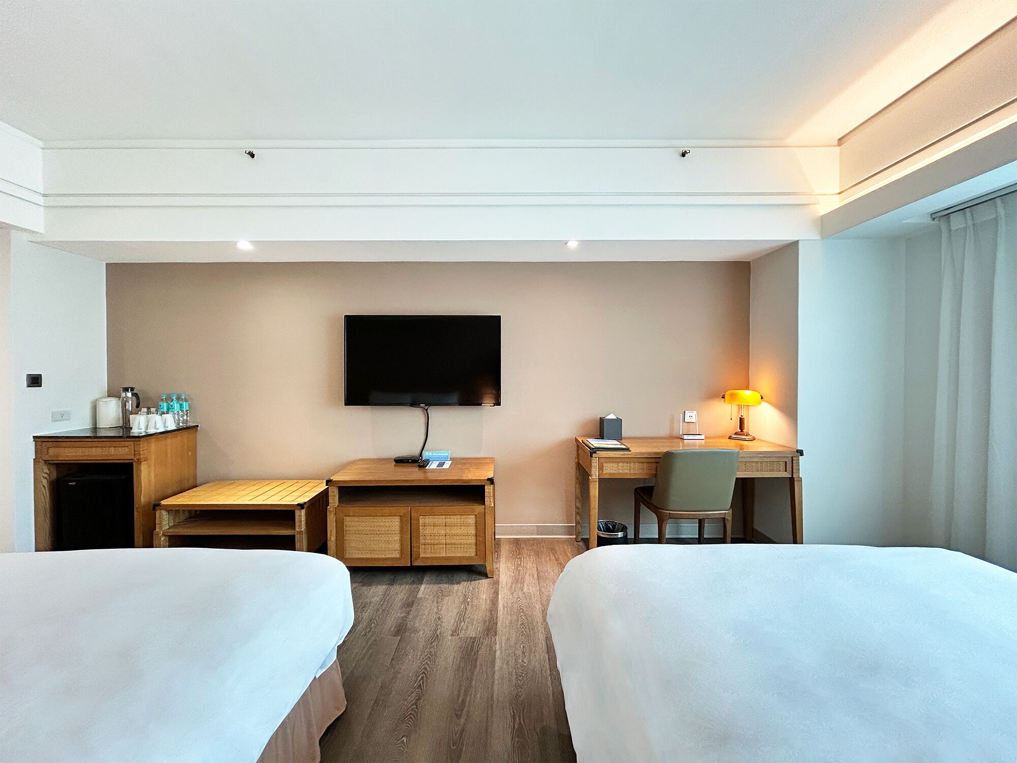 A hotel room with two beds, a desk, a TV, a lamp, and a minibar.
