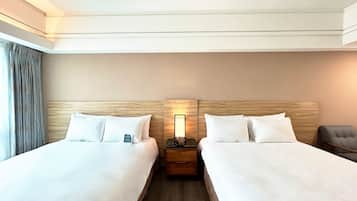A hotel room with two beds, a nightstand, a lamp, and a chair.