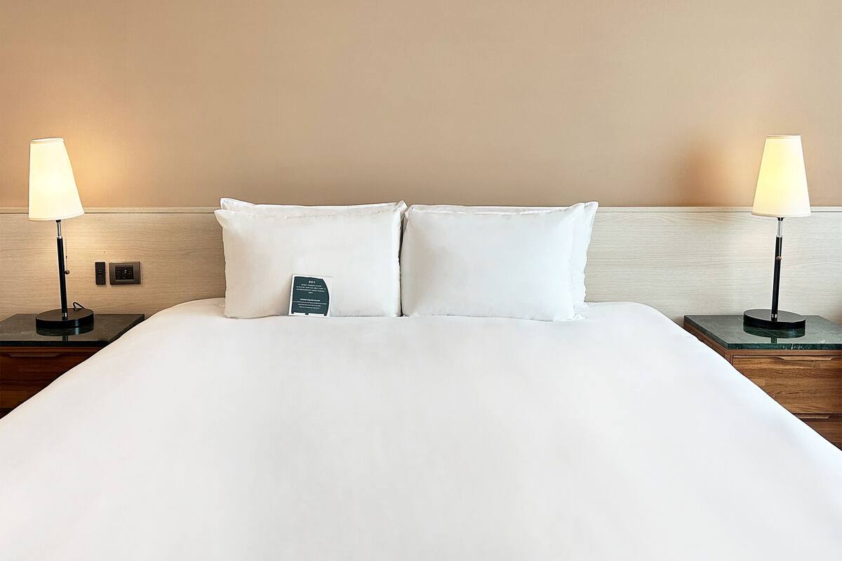 A hotel room with a large bed, two bedside lamps, and a nightstand with a lamp.