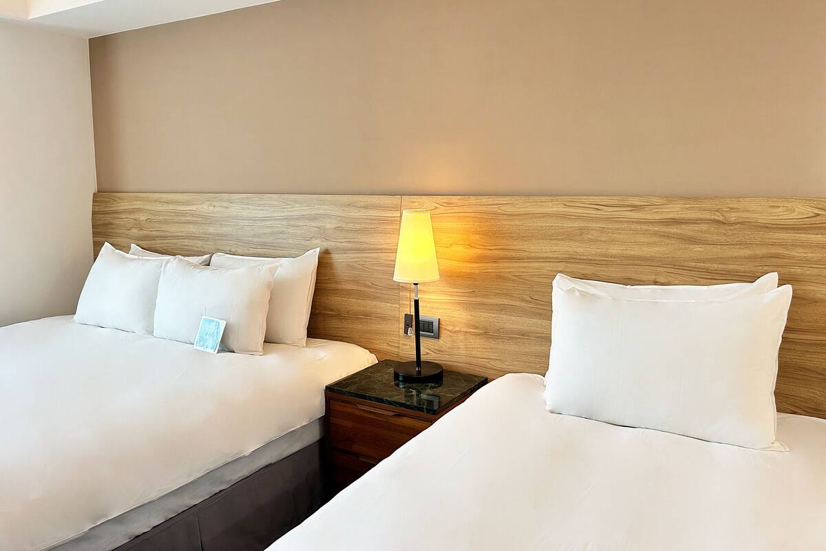A hotel room with two beds, a wooden headboard, a nightstand with a lamp, and a small table.