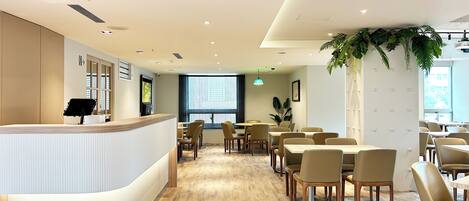 A modern hotel lobby with a reception desk, seating area, and large windows.