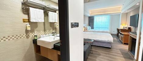 A hotel room with a bathroom, a bed, a desk, and a TV.