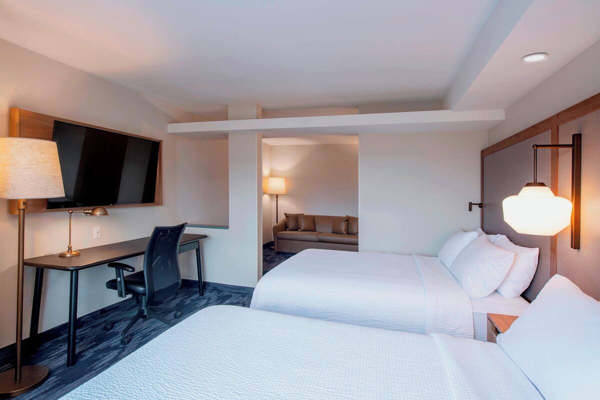 Une chambre d’hôtel avec deux lits, un bureau, une chaise, une télévision et une lampe.