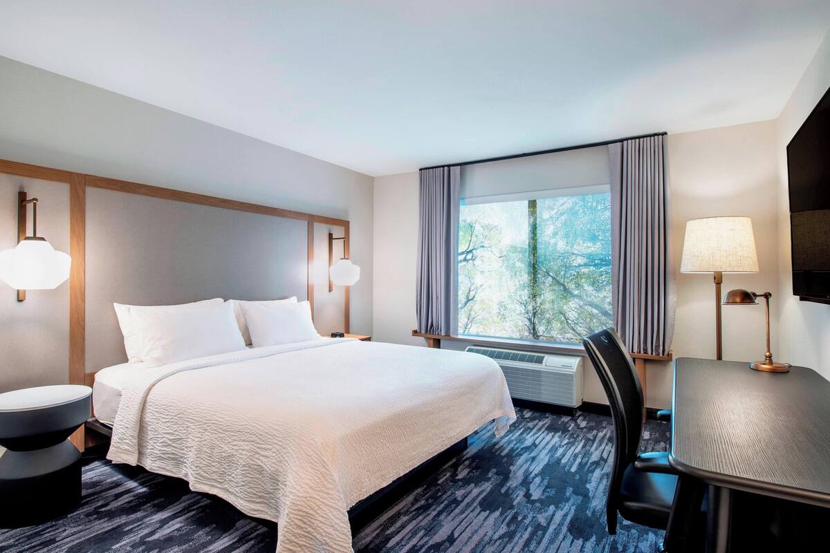 Une chambre d’hôtel avec un grand lit, un bureau, une chaise et une fenêtre avec des rideaux.