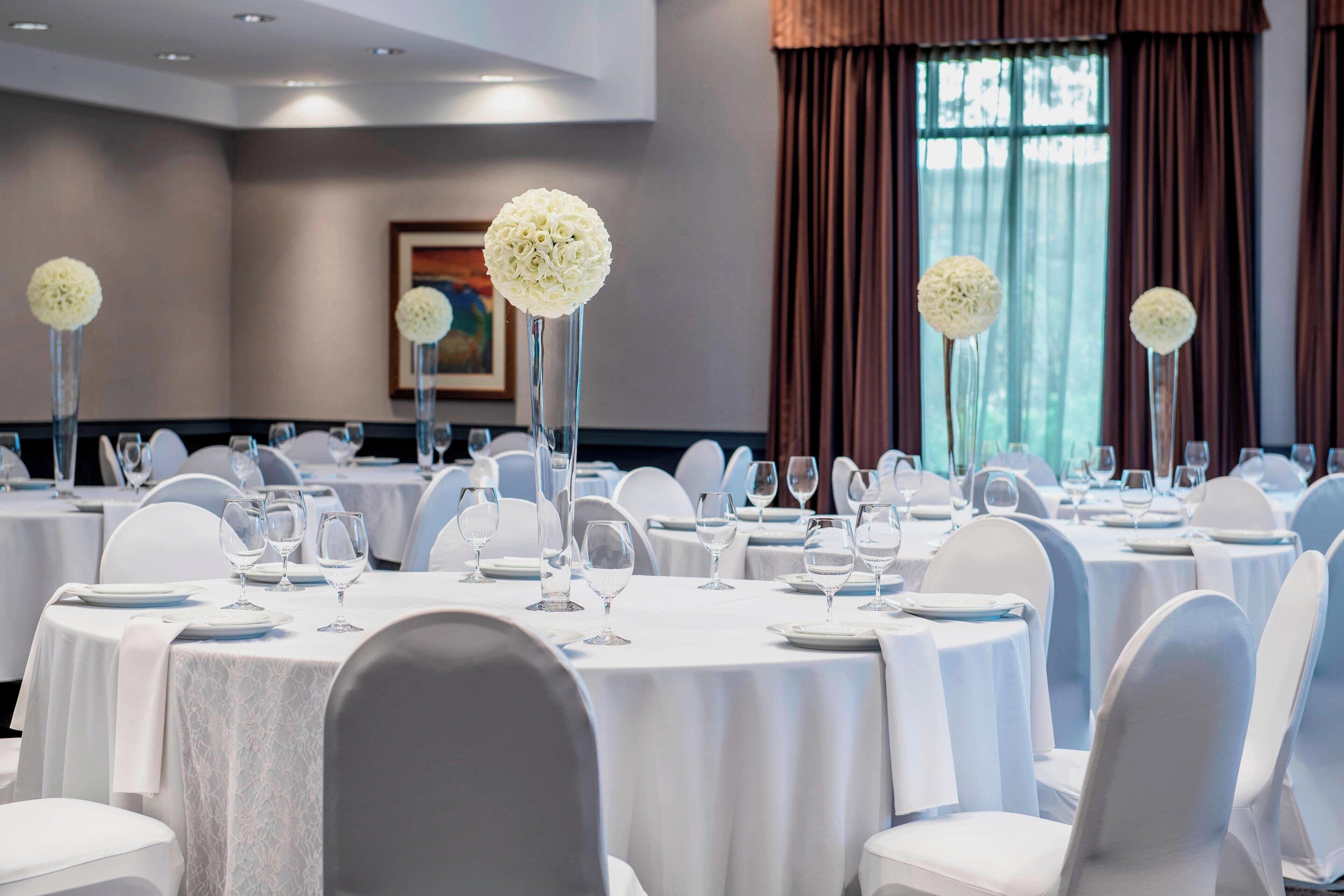 A banquet hall with round tables, white chairs, and floral centerpieces.
