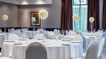 A banquet hall with round tables, white chairs, and floral centerpieces.