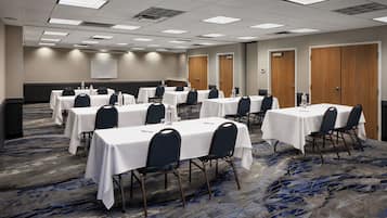 A conference room with multiple tables and chairs, carpeted flooring, and a projector screen on the wall.