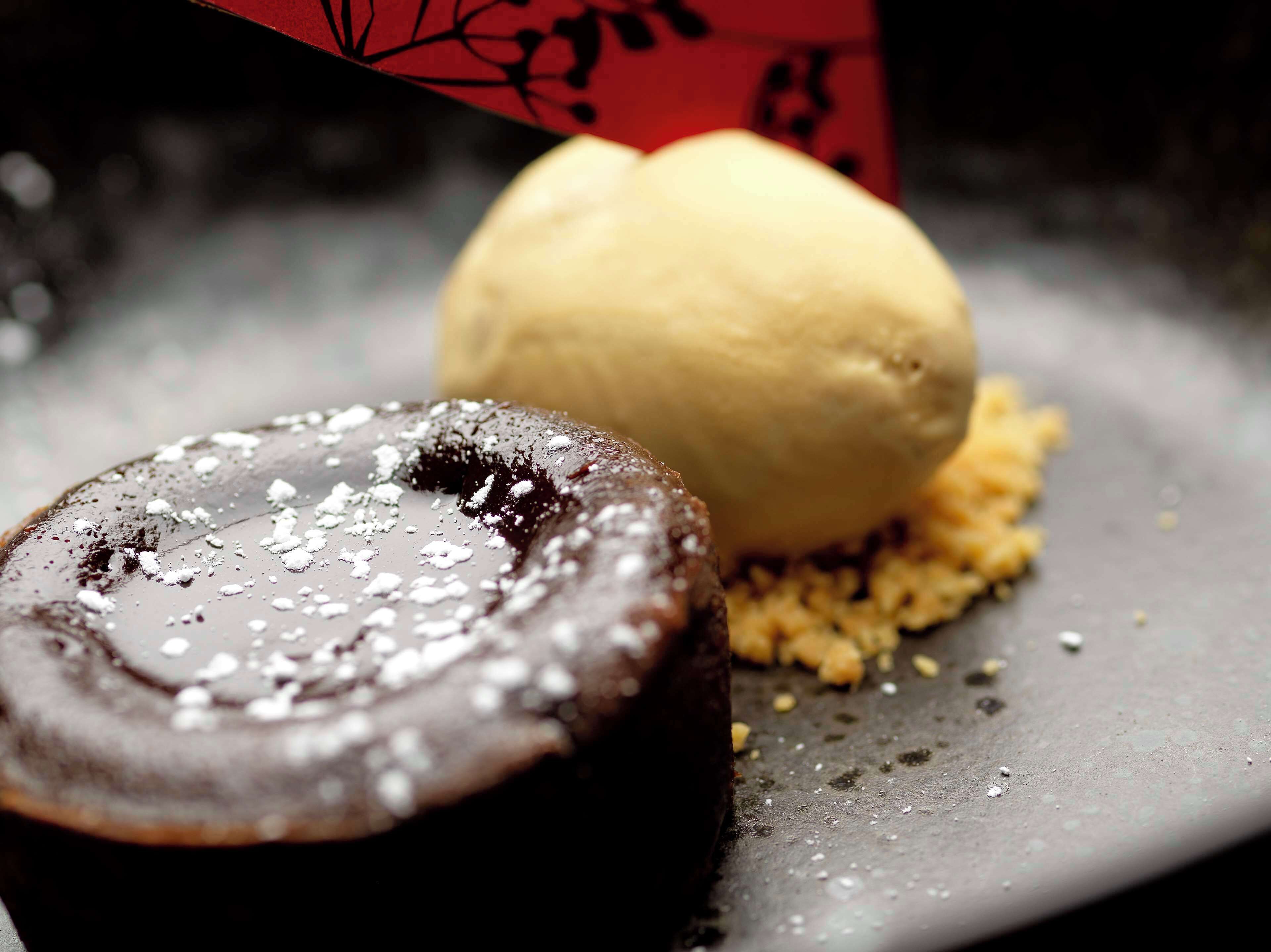 Un dessert composé d’un gâteau au chocolat et d’une boule de glace à la vanille, le tout servi sur une assiette parsemée de miettes.