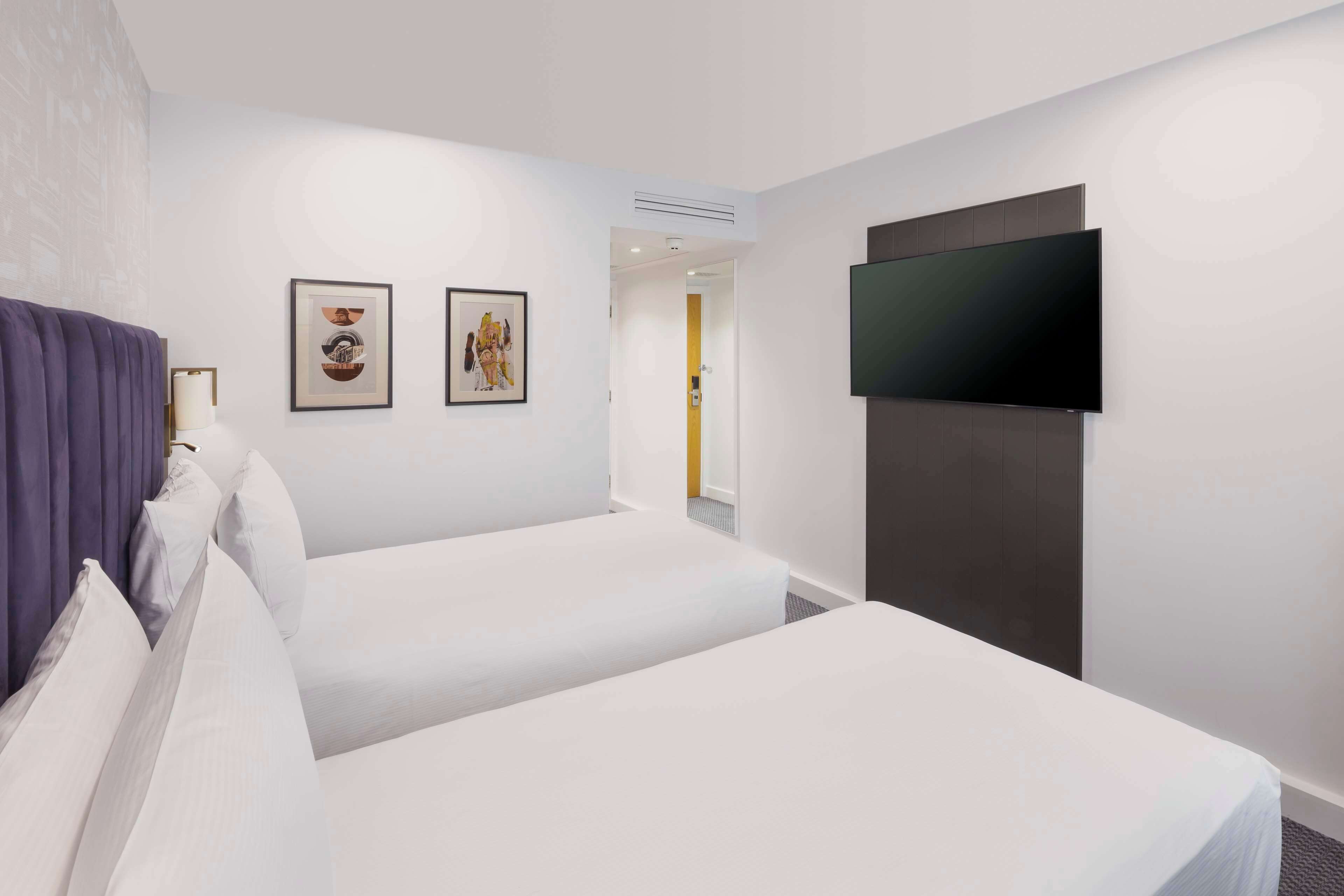 A hotel room with two beds, a flat-screen TV mounted on the wall, and two framed pictures on the wall.