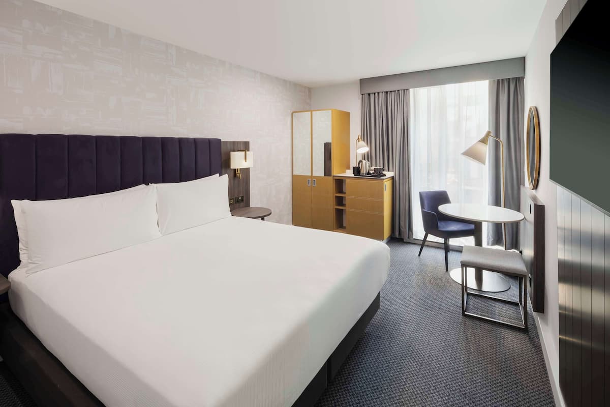Ein Hotelzimmer mit einem großen Bett, einem Schreibtisch, einem Stuhl, einem kleinen Tisch und einem Spiegel.