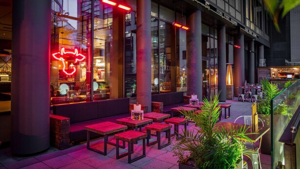 Un espace extérieur aménagé avec des tables et des chaises, de grandes colonnes et un panneau lumineux au néon.