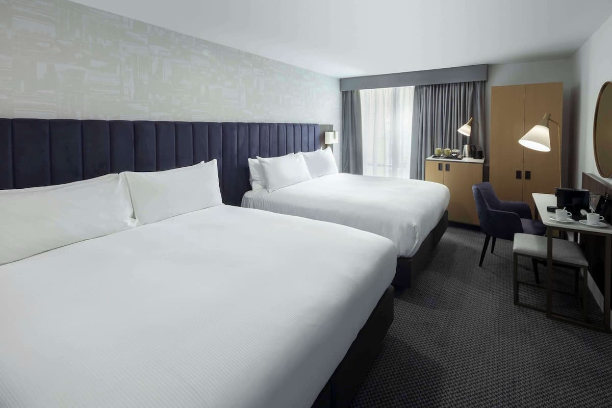 Ein Hotelzimmer mit zwei Betten, einem Schreibtisch mit Stuhl, einer Lampe und einem großen Spiegel.