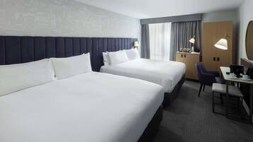 A hotel room with two beds, a desk with a chair, a lamp, and a large mirror.