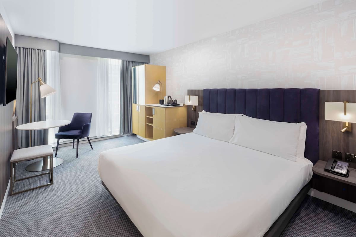 Ein Hotelzimmer mit einem großen Bett, einem Schreibtisch, einem Sessel, einem Fernseher und einer Minibar.